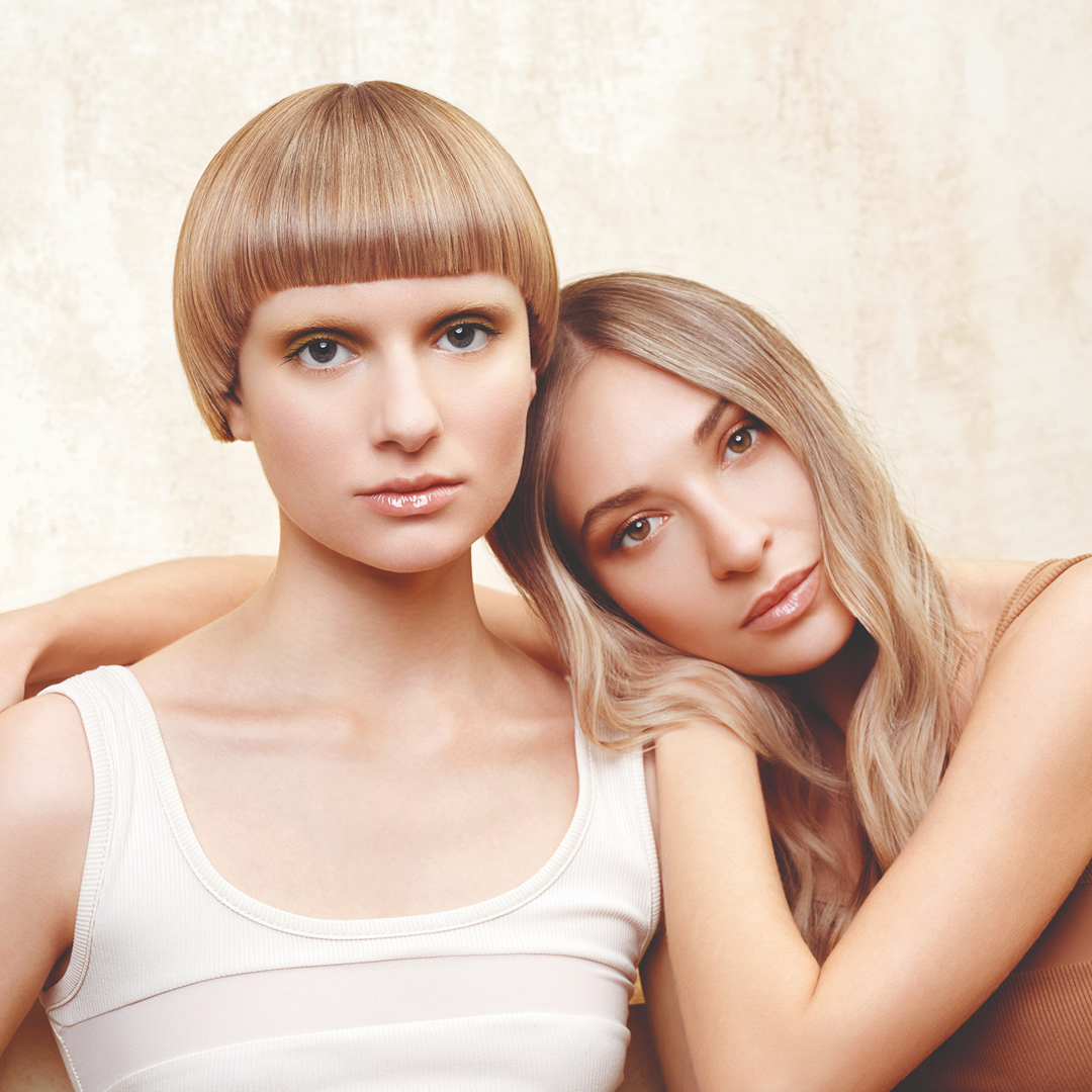 Immagine di due ragazze, una bionda con caschetta a sinistra e l'altra a destra, appoggiata sulla spalla dell'altra, sempre bionda con capelli lunghi